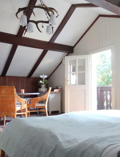 Schlafzimmer mit großem Bett, hellblauer Bettdecke, kleinem blauen Tisch und Rattanstühlen, offene Balkontür