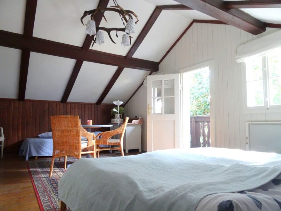 Schlafzimmer mit großem Bett, hellblauer Bettdecke, kleinem blauen Tisch und Rattanstühlen, offene Balkontür